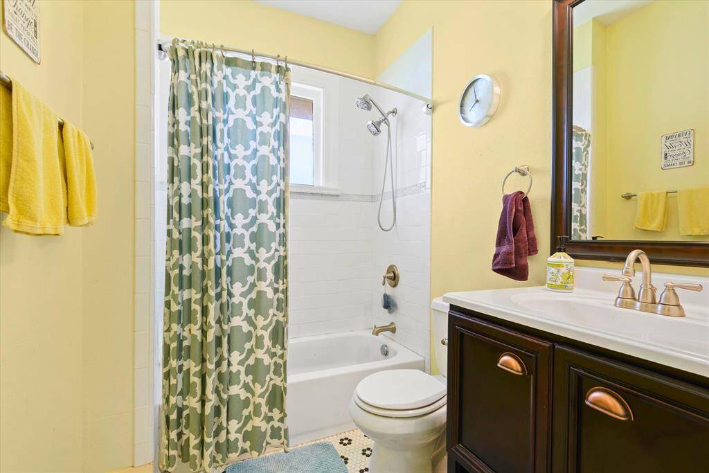 Bright and inviting, this full secondary bathroom offers a sleek vanity with ample storage, a dual-head shower over tub, and stylish bronze hardware throughout. Timeless white tile and patterned flooring add a touch of classic appeal