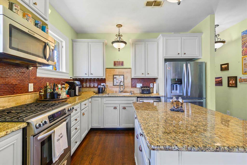 This kitchen features elegant white cabinetry, granite countertops, and stainless steel appliances. The space is accented with a warm backsplash and has an inviting island for additional prep, complemented by wood flooring and soft lighting.