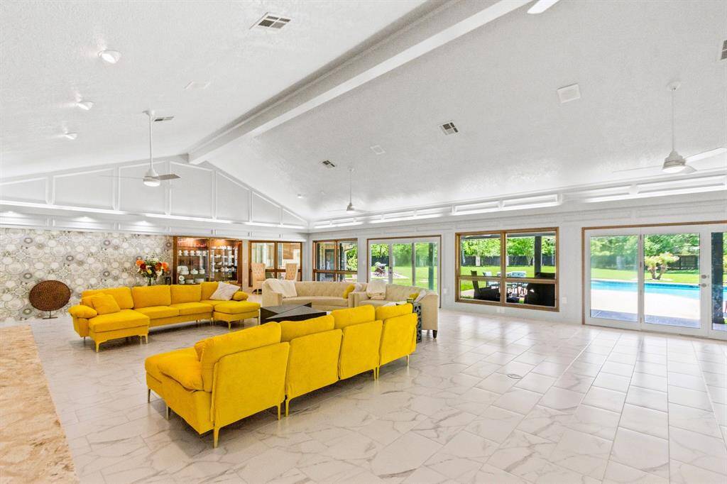 The living room features sleek floors, a grand stone fireplace, and soaring ceilings, all overlooking a spacious backyard.