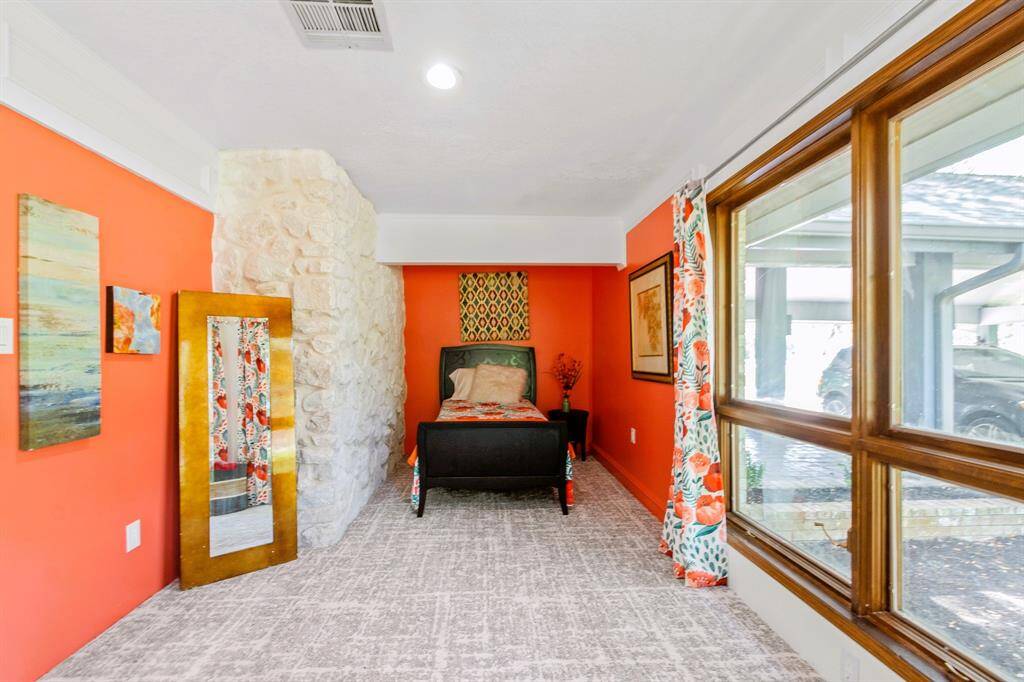 This bedroom features a striking stone wall, with large windows facing the front of the house, filling the space with an abundance of natural light.