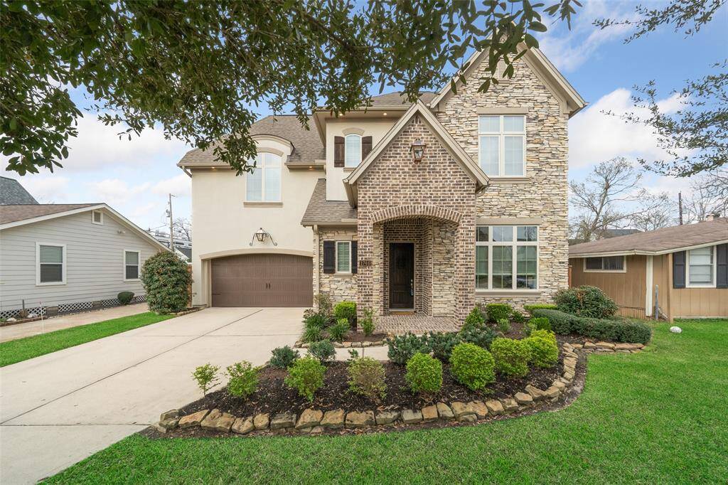 Stunning exterior elevation featuring a beautiful blend of brick, stone, and stucco, complemented by solid wood doors and charming wooden shutters. The double driveway offers ample parking, while the professional landscaping enhances the home's curb appeal.
