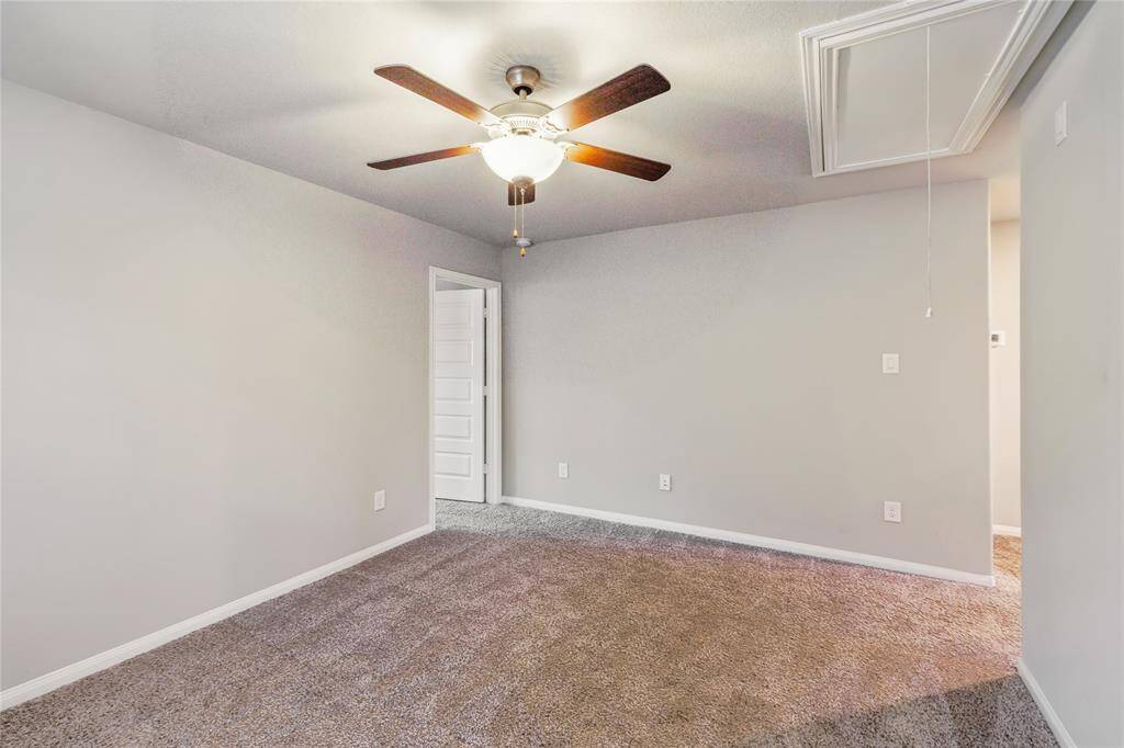 This room features neutral walls, plush carpeting, and a ceiling fan with light. A door leads to an adjacent space, creating a cozy and inviting atmosphere.