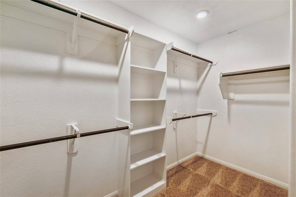 Spacious walk-in closet with multiple hanging rods and built-in shelves, providing ample storage. The carpeted floor adds warmth, and recessed lighting ensures good visibility.
