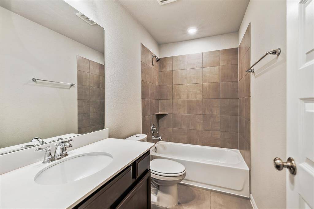 This is a modern bathroom featuring a sleek vanity with a white countertop and under-mount sink, complemented by a large mirror. The shower-tub combo is surrounded by stylish brown tiles, and the space is well-lit with recessed lighting.