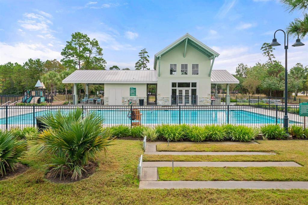 This serene outdoor space features a circular concrete patio with a central fire pit, surrounded by benches and lush greenery. It's set alongside a tranquil pond, offering a peaceful retreat.