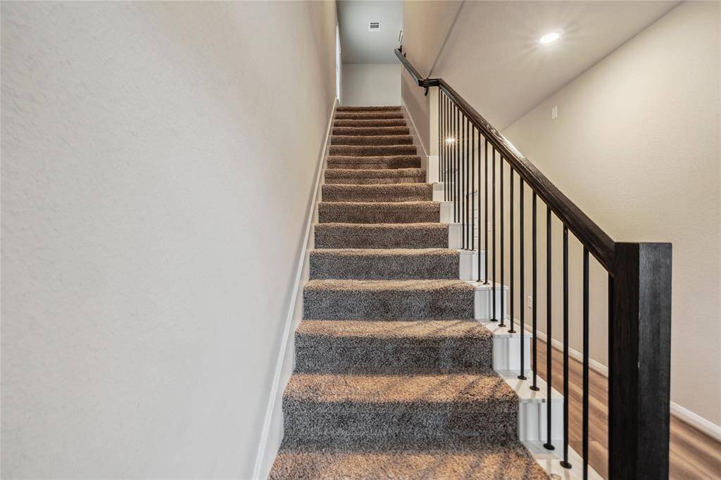 Staircase with a sleek black railing, leading to the upper floor. The walls are painted in a neutral tone, and recessed lighting provides a warm ambiance.