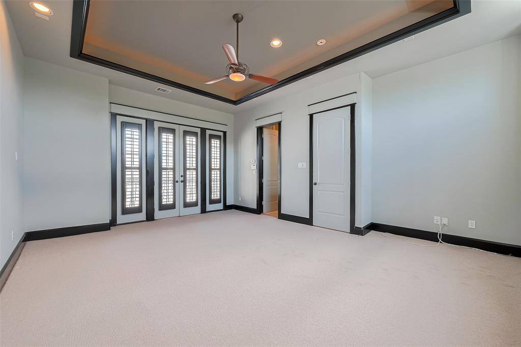 Lovely and expansive, the primary suite exudes comfort with a striking tray ceiling, soft neutral hues, and bold, dark trim. Double doors with sidelights open to a private balcony, while recessed lighting adds warmth and dimension.