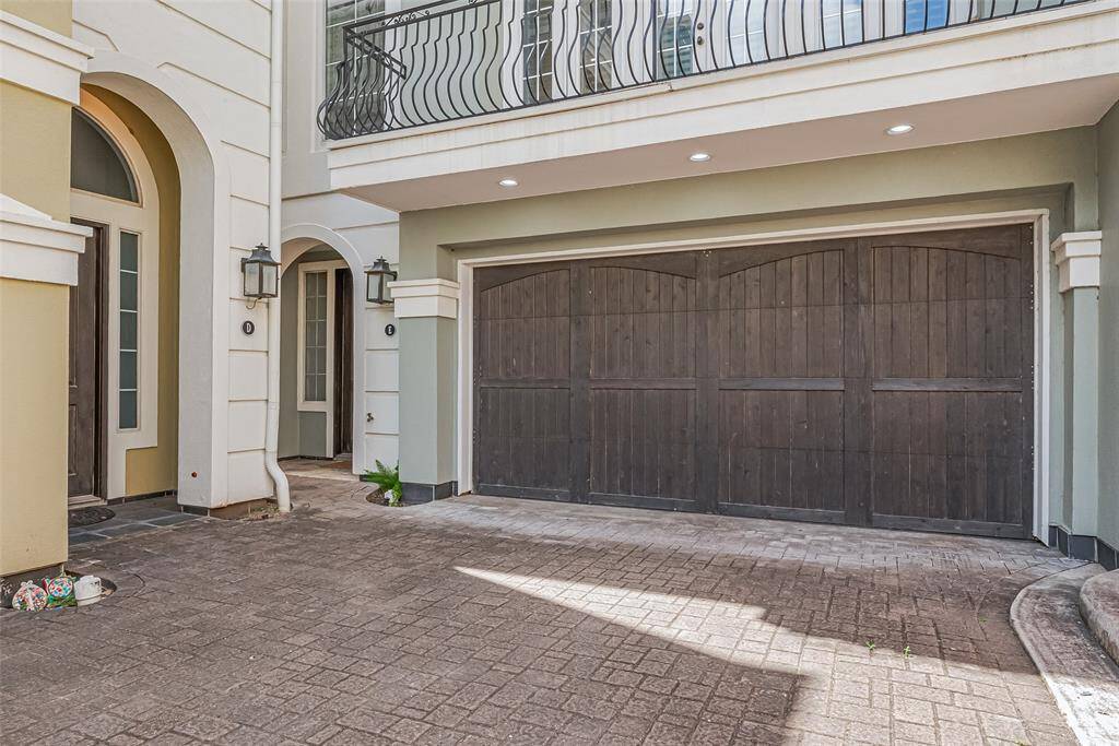 Dark-toned wooden doors shine under soft recessed lighting from the balcony above, creating a welcoming and polished entry for the two-car garage.
