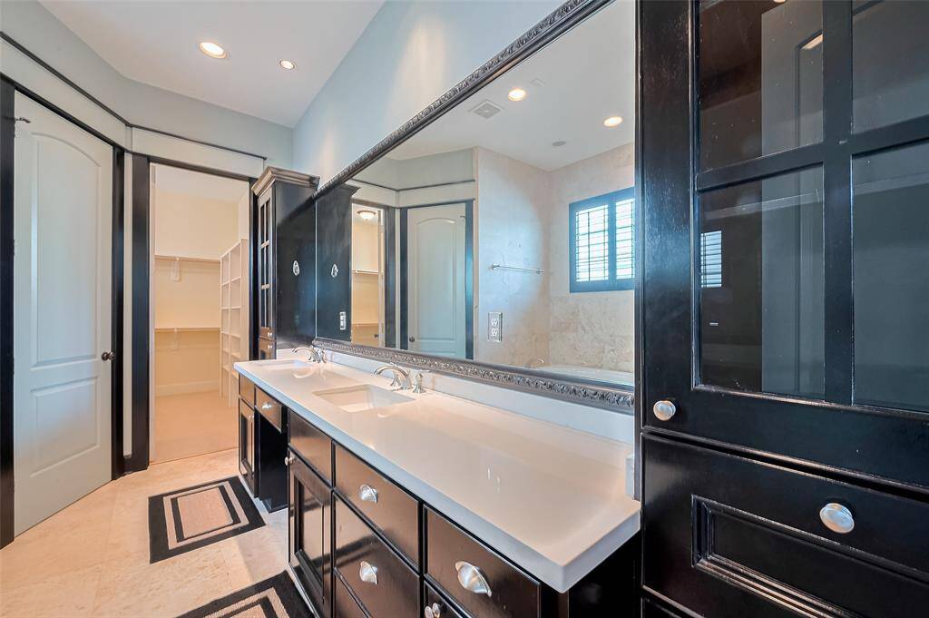 A luxurious haven, the primary bath showcases a dual-sink vanity topped by an oversized mirror and flanked by rich cabinetry. A soaking tub invites relaxation, with a spacious closet just beyond.