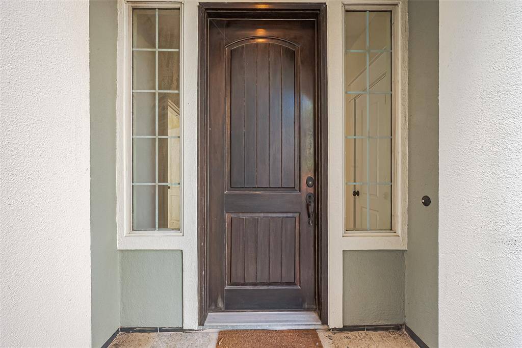 Tucked beneath a graceful archway, the front door makes a bold first impression with rich wood tones framed by glass sidelights.
