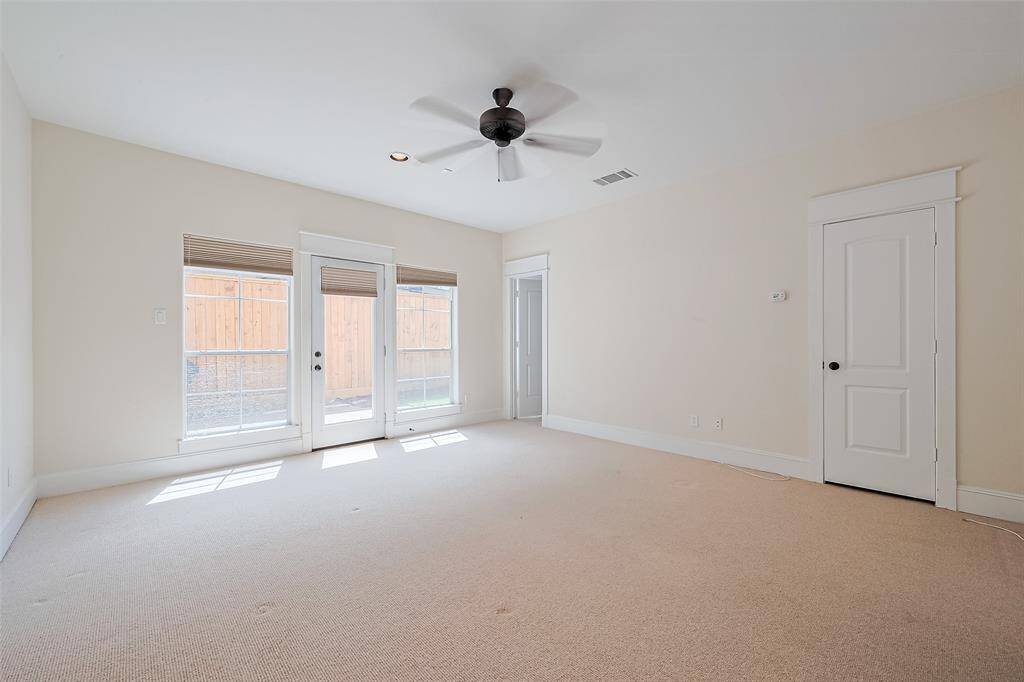 This generously sized bedroom on the first floor offers plush carpeting, a ceiling fan, and an abundance of light from large windows that flank a glass-paneled door leading to the backyard—ideal for guest use.