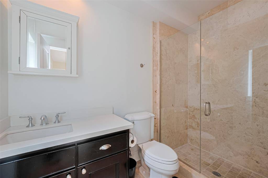 A refined en suite bath complements the first-level bedroom with a stylish vanity offering under-sink storage, paired with a glass-enclosed shower in a crisp, modern design.