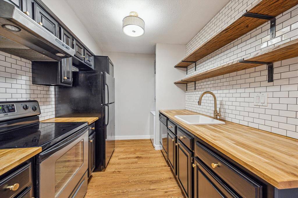 Stylish kitchen with butcher block counters, subway tile backsplash, open shelving and black painted cabinets with gold hardware. Plenty of space to prep your favorite meals!