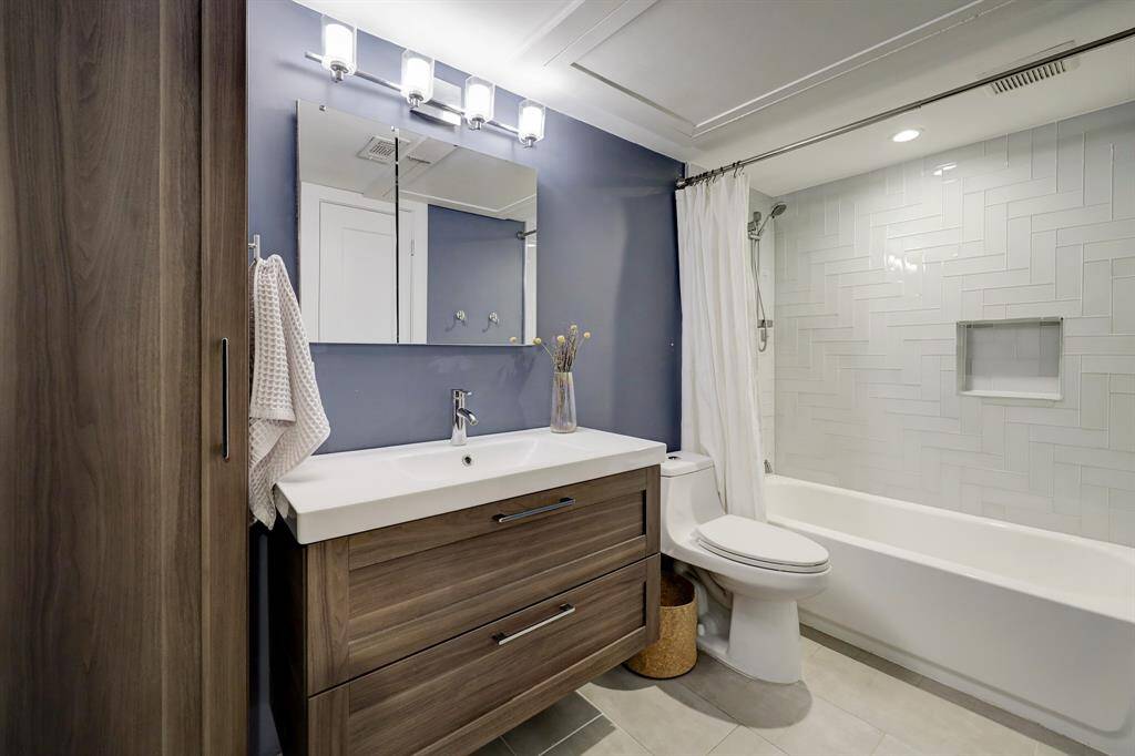Updated bathroom with furniture style vanity and tub/shower with glass tile in intricate pattern.