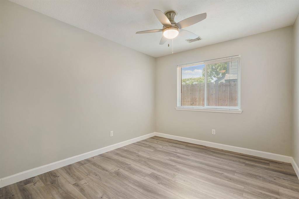 This room features neutral walls and wood-style vinyl flooring, accented by a ceiling fan and a window providing natural light.