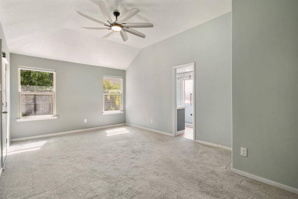 This spacious primary bedroom features soft carpet and ample natural light from two large windows. It includes a ceiling fan and an ensuite bathroom for added convenience.