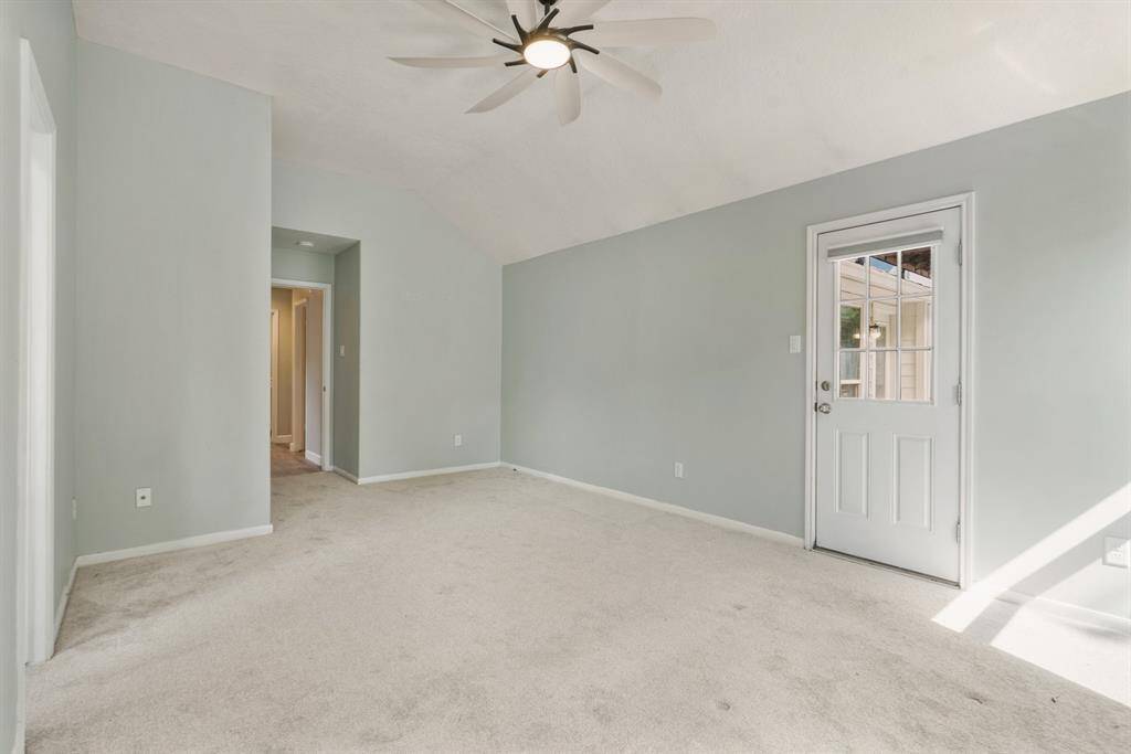 Bright, spacious primary bedroom with carpet, featuring a ceiling fan and a door leading to the outside backyard.