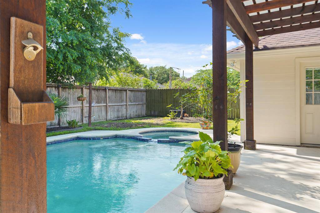 This backyard features a serene swimming pool  with attached hot tub set in a cozy patio area, surrounded by a wooden fence and lush greenery, perfect for relaxation and outdoor enjoyment.