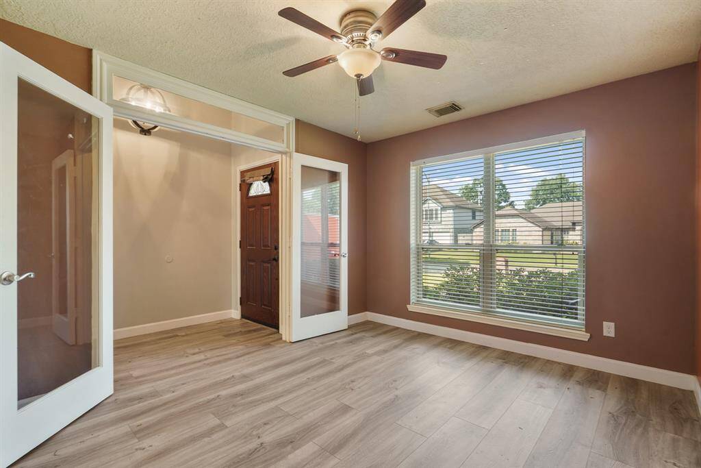 Formal dining room with ceiling fan, located to the left of the foyer. Features double doors for privacy and a view of the front yard.