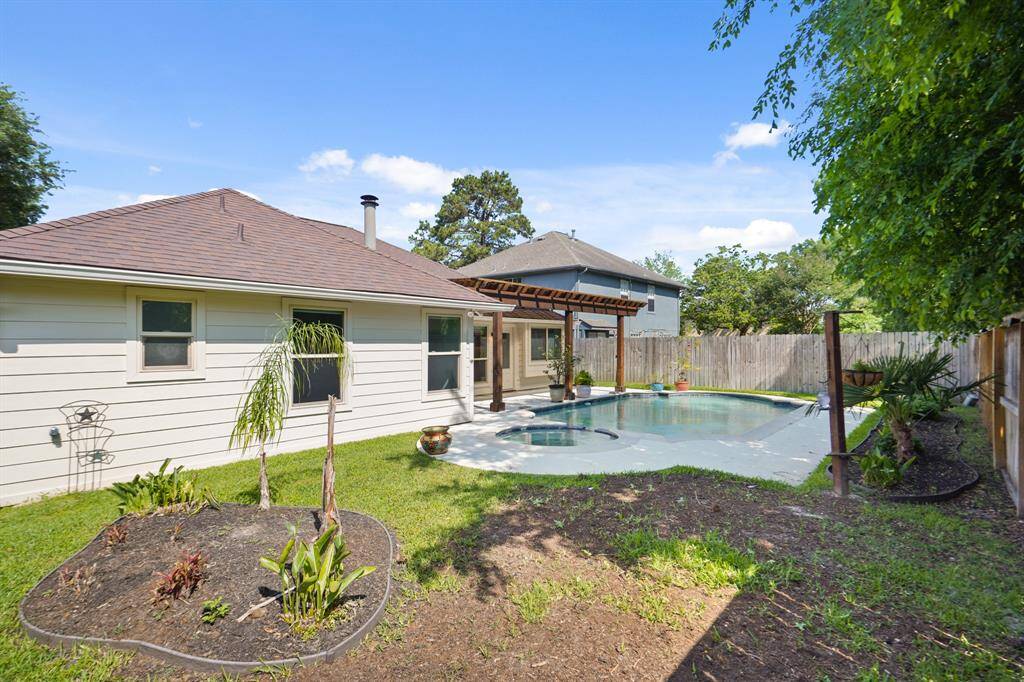 Charming backyard with a covered patio and a private pool with attached hot tub, surrounded by a wooden fence and lush greenery, ideal for relaxation and entertainment.