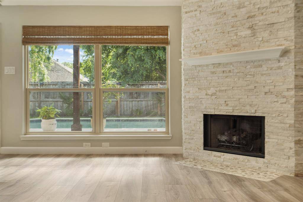 Bright living space featuring a large window with a view of a backyard underground pool, complemented by a stylish stone fireplace and light wood vinyl flooring.