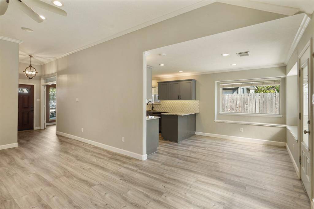 This photo showcases a bright, open-concept space showing the connections between the living area, kitchen and breakfast nook. The rooms features light wood vinyl flooring, neutral walls, and recessed lighting. The kitchen area includes sleek cabinetry and a stylish backsplash.