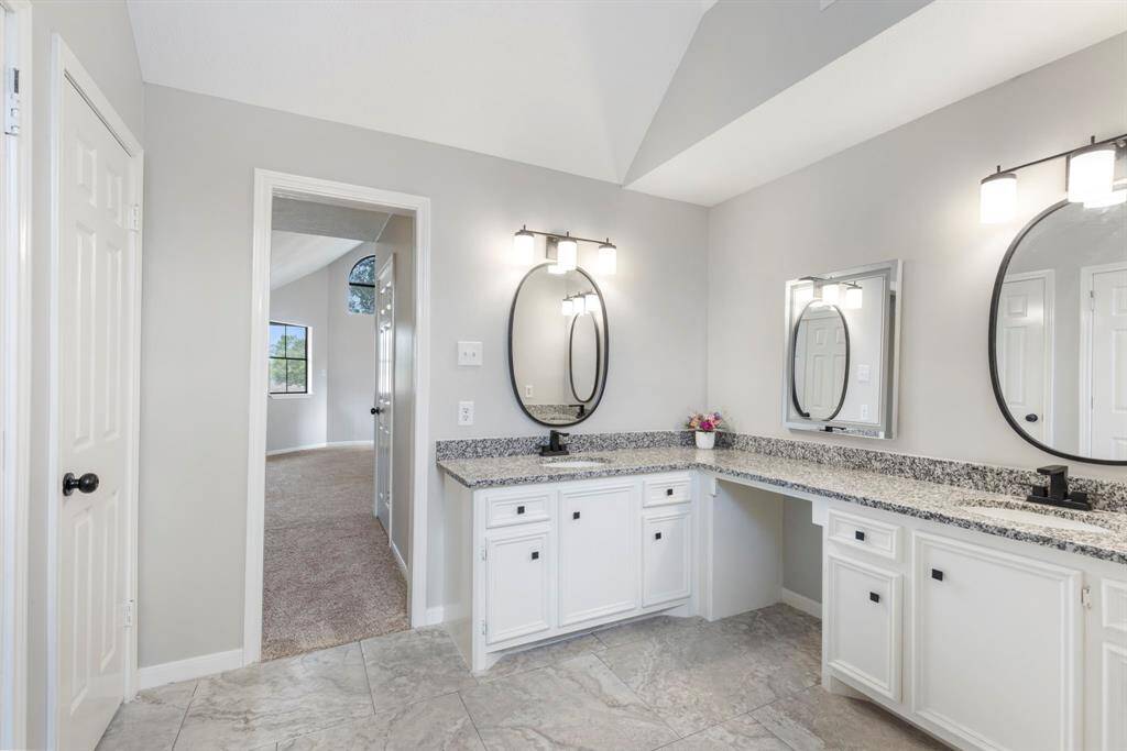The spacious, updated primary bathroom boasts with granite countertops, dual sinks, and modern fixtures