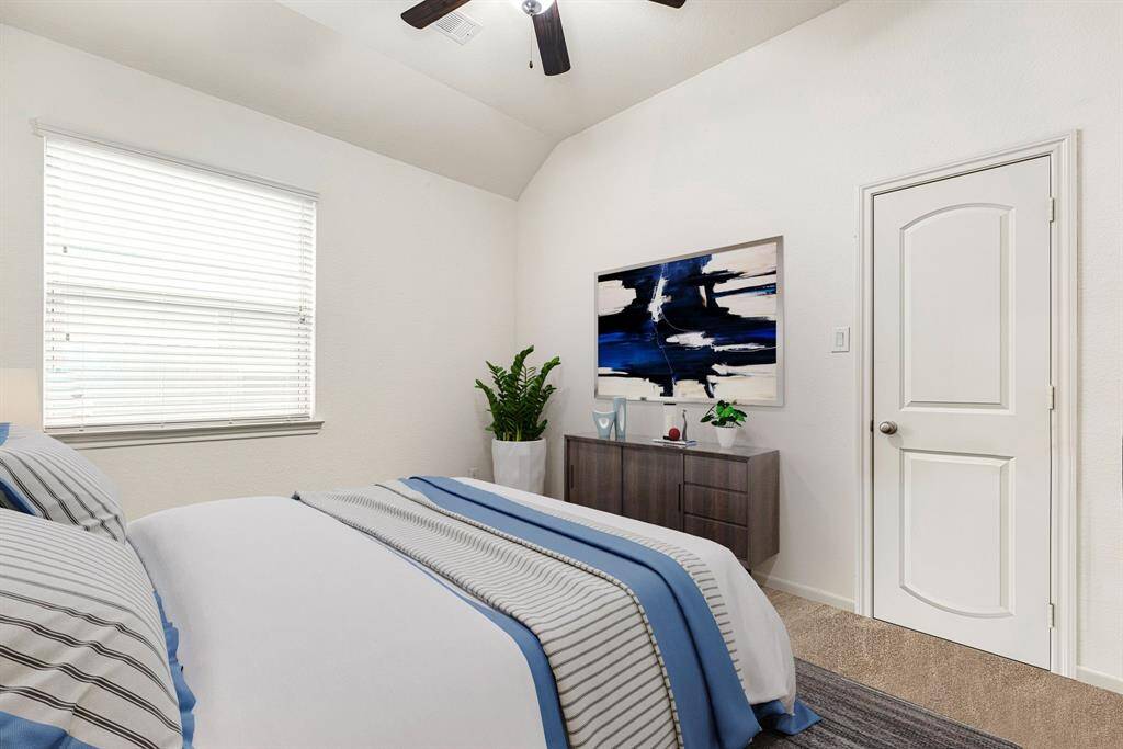 Secondary bedroom features plush carpet, neutral paint, dark stained ceiling fan with lighting and a large window with privacy blinds.