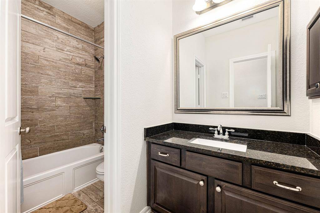 Secondary bathroom features granite countertops and dark cabinets, neutral paint, shower/tub combo with tile surround, large mirror, tile floors, sleek fixtures and modern finishes, plenty of space to accommodate any visiting family or guests.