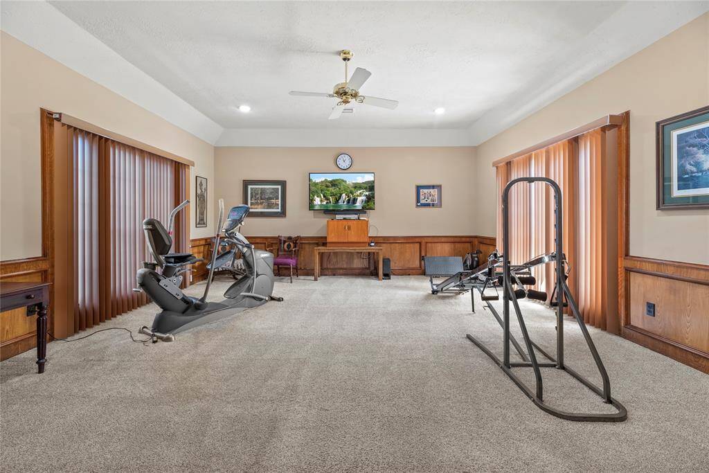 Spacious home gym and game room measures 21 x 18 with carpeted floors, a ceiling fan, and large windows that bring in plenty of natural light. This versatile space can easily be transformed into a family room, home office, theater room, or anything you envision!