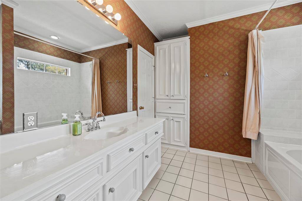 Second bedroom bathroom featuring a double vanity with white cabinetry, elegant wallpaper, and a large mirror. The room includes a bathtub and a window providing natural light.