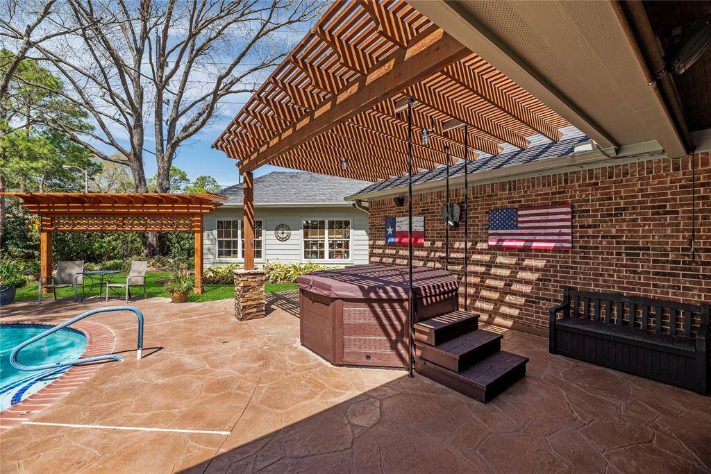 Backyard features a spacious patio with a hot tub under a wooden pergola, adjacent to a swimming pool. The area is perfect outdoor retreat.