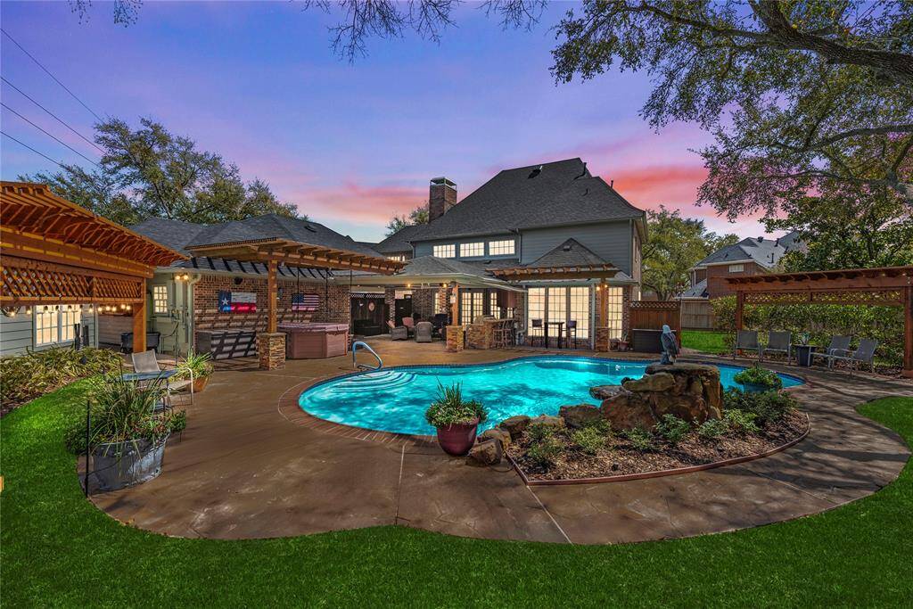 Backyard twilight view showcasing the home's stunning architecture, with a covered and spacious patio perfect for relaxing, grilling, and entertaining. The warm lighting enhances the inviting atmosphere, making it an ideal spot for evening gatherings.