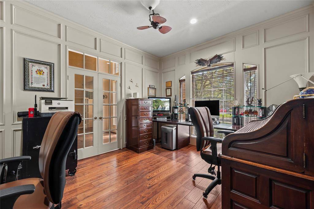 Home office measures 12.7 x 14.9 features elegant wood paneling, a ceiling fan, and ample natural light through large windows.