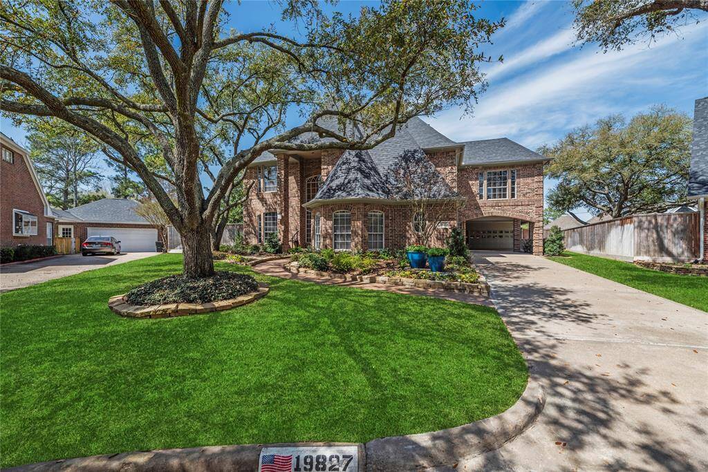 Charming two-story home with a well-maintained lawn and mature trees. The property features a spacious driveway leading to a two-car garage.