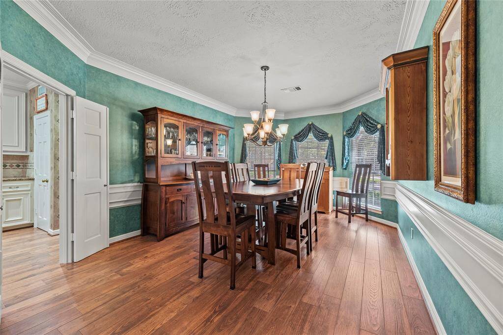 Dining room features natural light from large windows viewing the front of the house and adorned with drapery. Warm wood flooring adds a perfect touch.