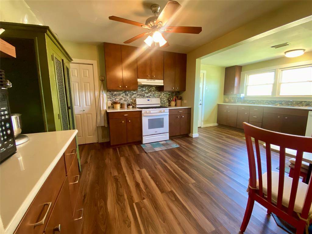 Spacious kitchen with rich wood cabinetry, modern appliances, and a stylish backsplash. The room features a ceiling fan and ample natural light, complemented by warm wood flooring.