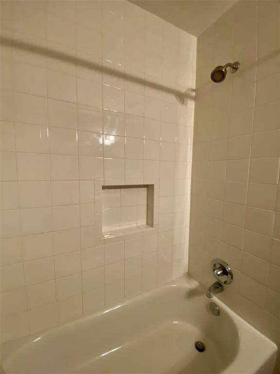 This photo shows a clean, tiled bathtub and shower area with a built-in shelf, featuring white tiles and chrome fixtures.