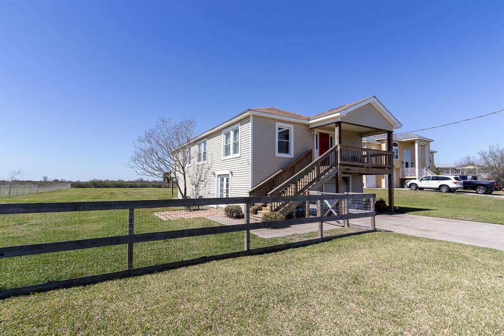 This property features a charming, elevated home with a spacious front yard and a long driveway. The 3/4 acre fenced yard offers privacy and ample space, with scenic views of open fields and views of Galveston's West Bay. Ideal for those seeking tranquility and room for outdoor activities.