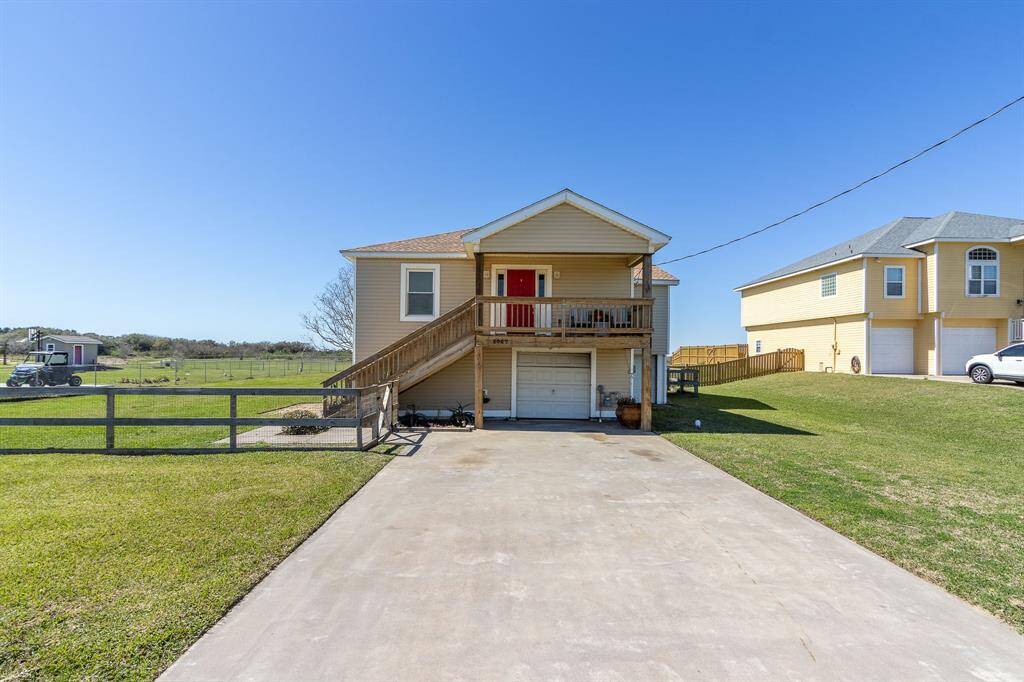 This elevated home features a wooden staircase leading to a welcoming red front door. It has a generous 2-car tandem garage and double wide driveway.
