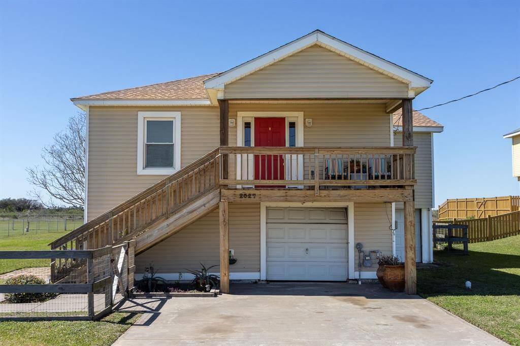 Charming raised home with a red front door, wooden porch, and staircase.