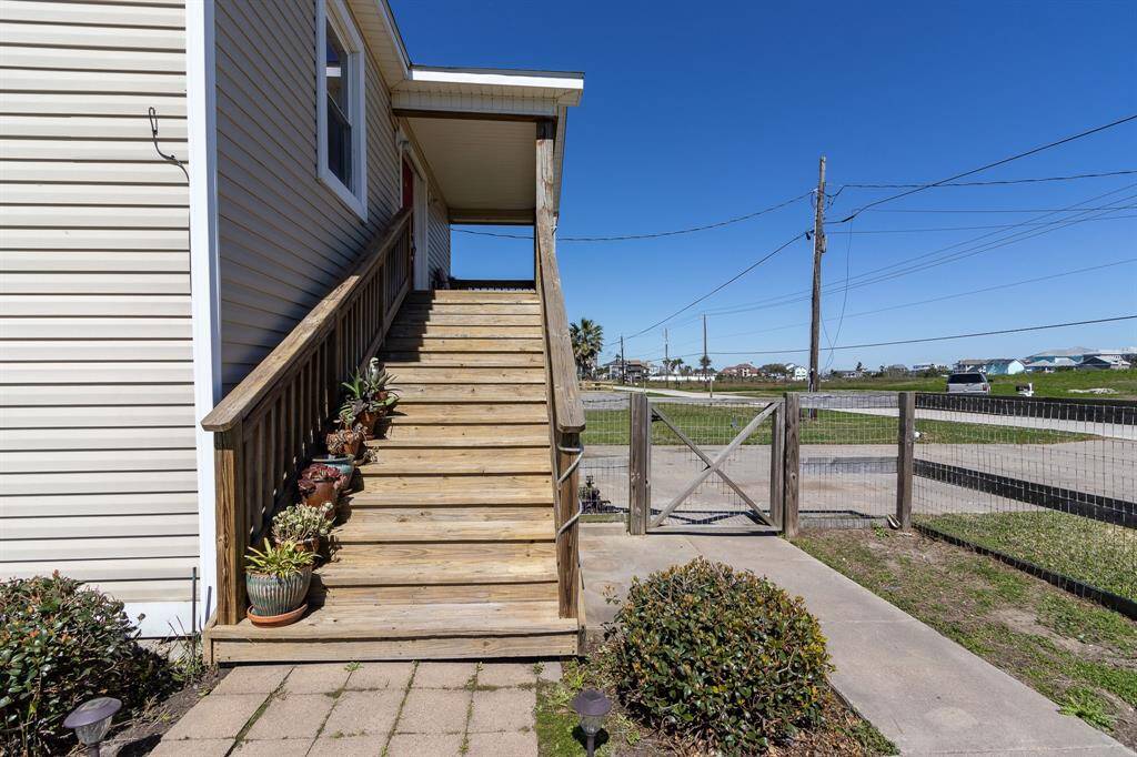 This photo shows an exterior view of the front wooden staircase leading to the front entrance. Front gate leads to the double wide driveway.
