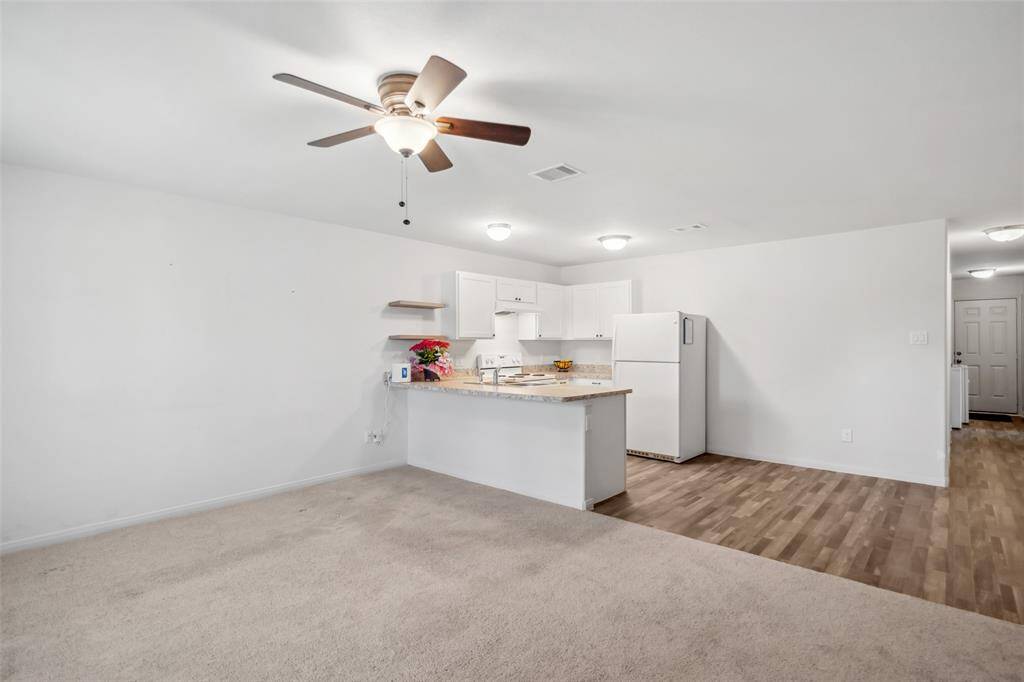 Bright and airy living space with view of the kitchen island, ceiling fan, and durable vinyl flooring in high-traffic areas.