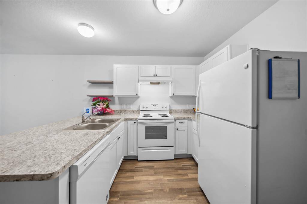 Functional and clean kitchen with ample cabinet space, laminate countertops, and matching white appliances. A window-like view opens directly into the living area.