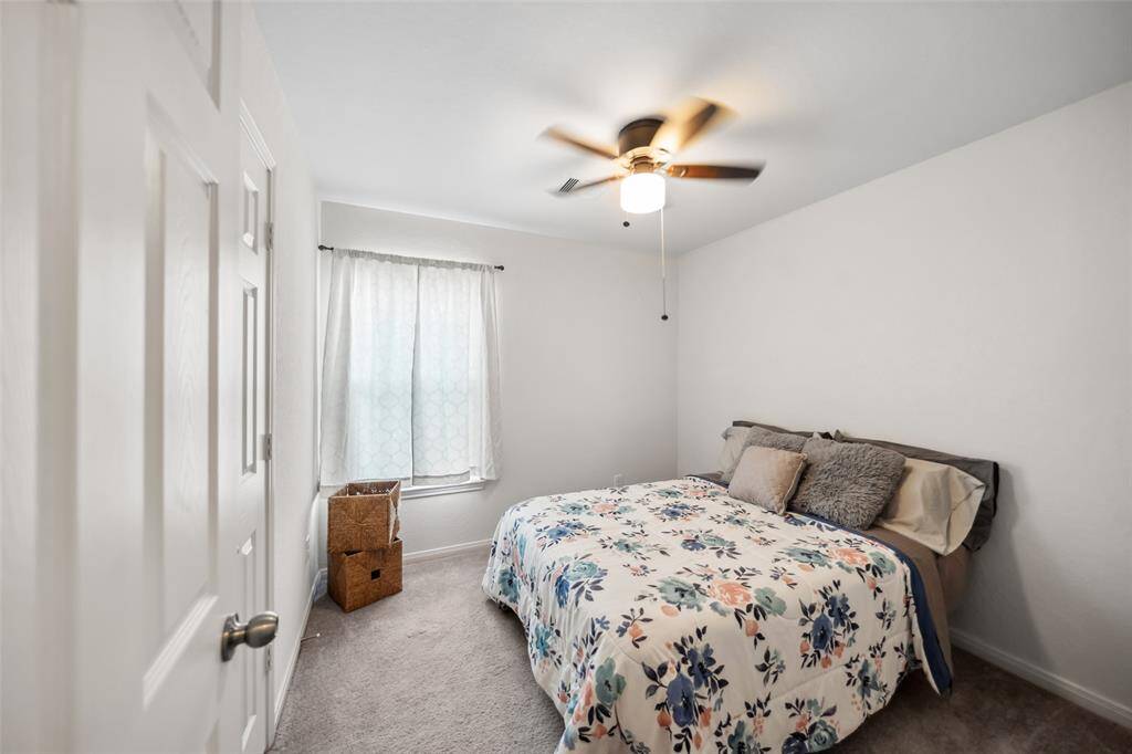 Cozy secondary bedroom with plush carpet, neutral tones, and soft natural light. Features a ceiling fan and ample space for a full-size bed setup.