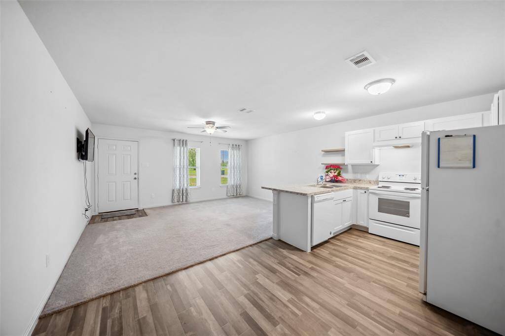 Bright and open living area flowing into the kitchen. Features include carpet and vinyl flooring, laminate countertops, white cabinetry, and included appliances—ideal for everyday living and entertaining.