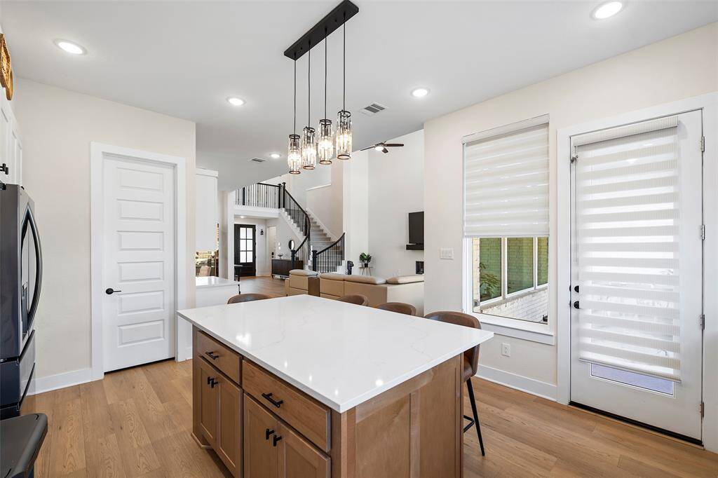 A view from the kitchen island highlights the home’s seamless layout and connection to the main living space. Note the curved staircase and soaring ceilings beyond—both adding architectural interest and a grand sense of scale.