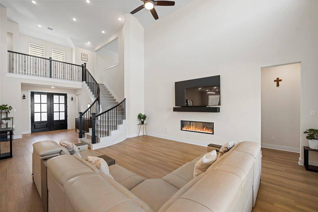 A dramatic curved staircase with wrought-iron spindles anchors the living room, complementing the soaring ceilings and drawing the eye to the home’s thoughtful architectural details.