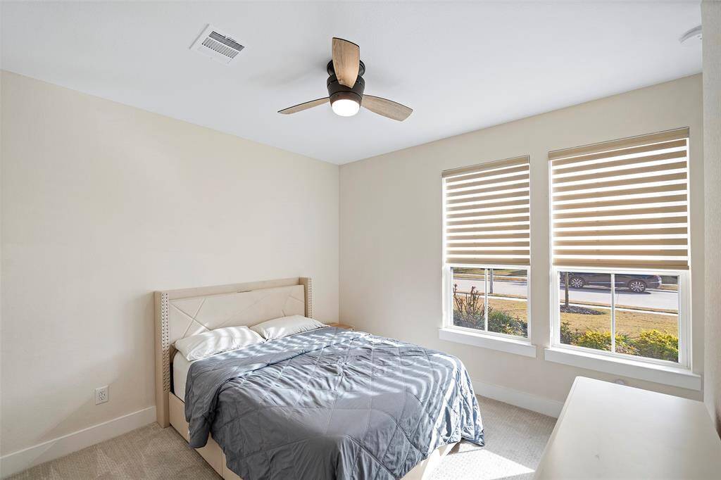 Natural light pours through dual front-facing windows in this first floor secondary bedroom, complemented by neutral tones and plush carpet underfoot. A modern ceiling fan adds comfort and style.