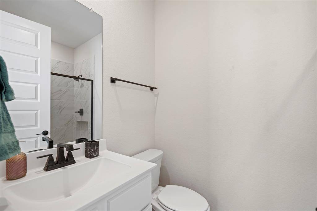 Secondary bathroom is finished in soft neutral tones and features a sleek vanity with dark hardware and coordinating fixtures. A tiled tub and shower combination can be seen just beyond the door, offering a versatile layout for guests or family members.